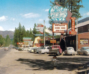 This photo likely was taken about 1956, as Heavenly Valley opened in 1955, and shows the two-lane Highway 50 towards the Nevada state line. The photographer likely took this image from where today would be in the middle of a Ski Run Boulevard turn lane next to today's Red Hut. The photo shows that there were no stoplights at south shore in the early 1950s. The Lawrence's Department Store sign (left-center) fronted the same building which was remodeled and now houses Chevy's Restaurant.
